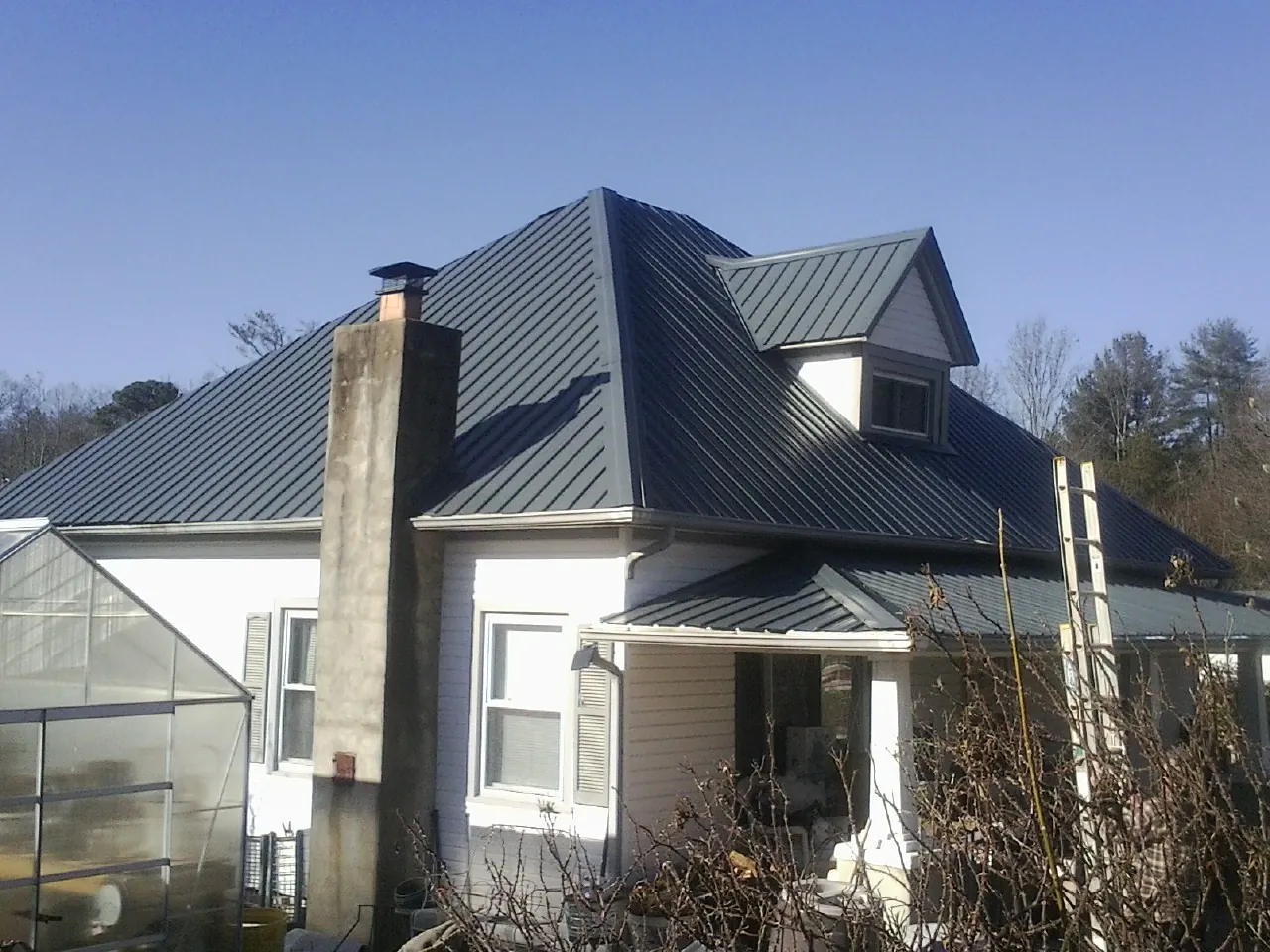 Dark blue standing seam metal roof on a white farmhouse with dormer — Slate & Tile Roof Repair by Roofing Brothers in Ira