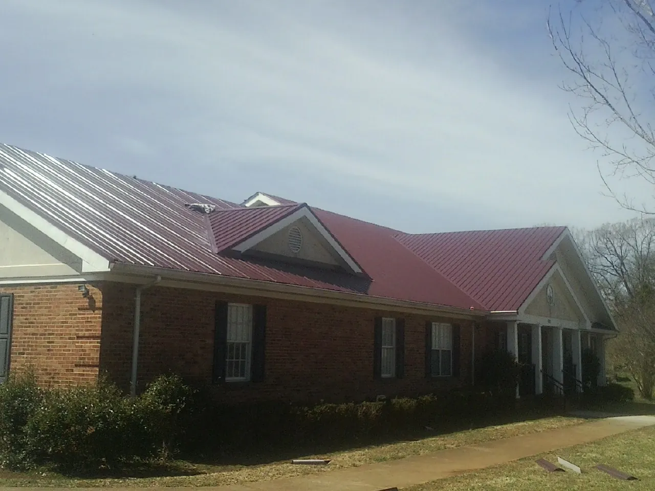 Red metal roof with gabled entries on a long brick building, from a Hail Damage Roof Repair job in Ira