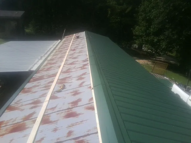 Old rusted panels beside newly installed green metal roofing — Wind Damage Roof Repair by Roofing Brothers in Ira