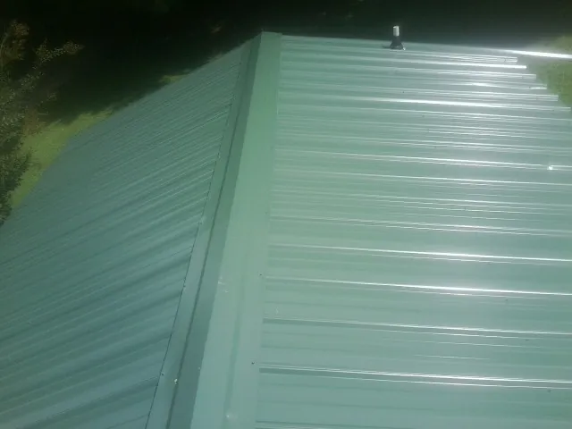 New green metal panels meeting at the ridge of a roof — Flat Roof Repair work by our crew in Ira