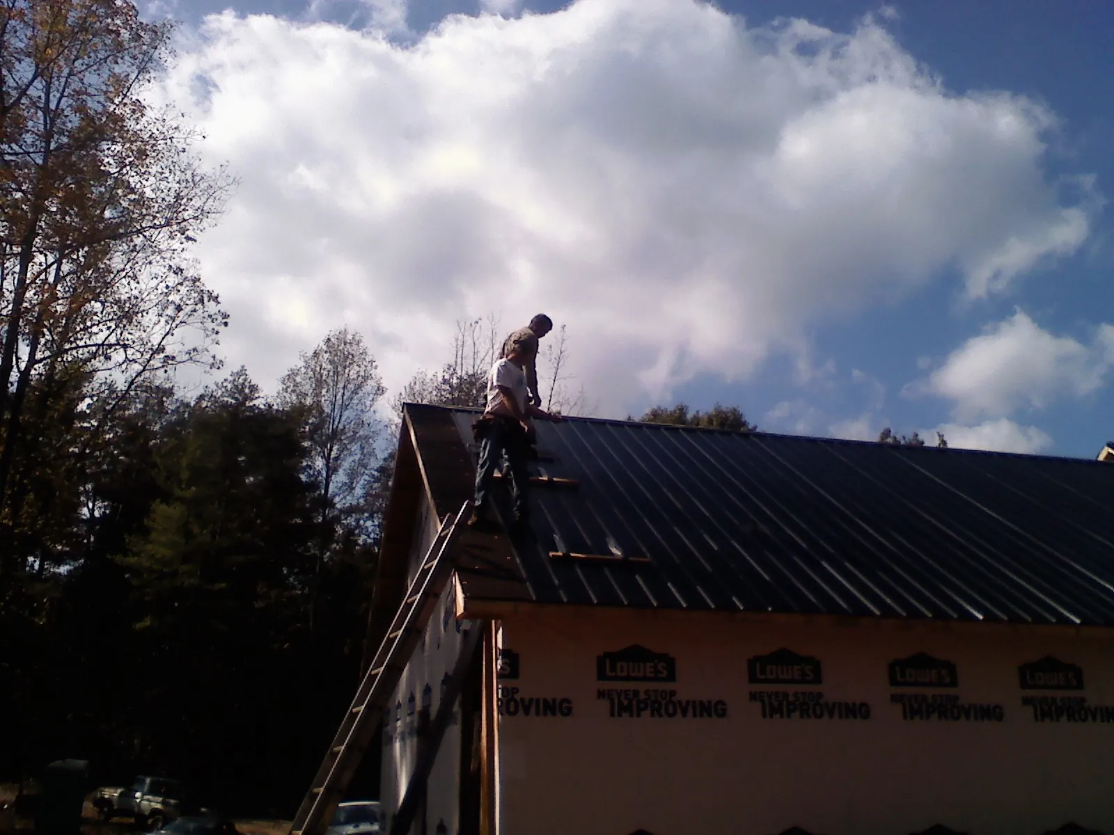 Roofer fastening dark metal panels high against a cloudy sky, from a Roof Inspection job in Ira