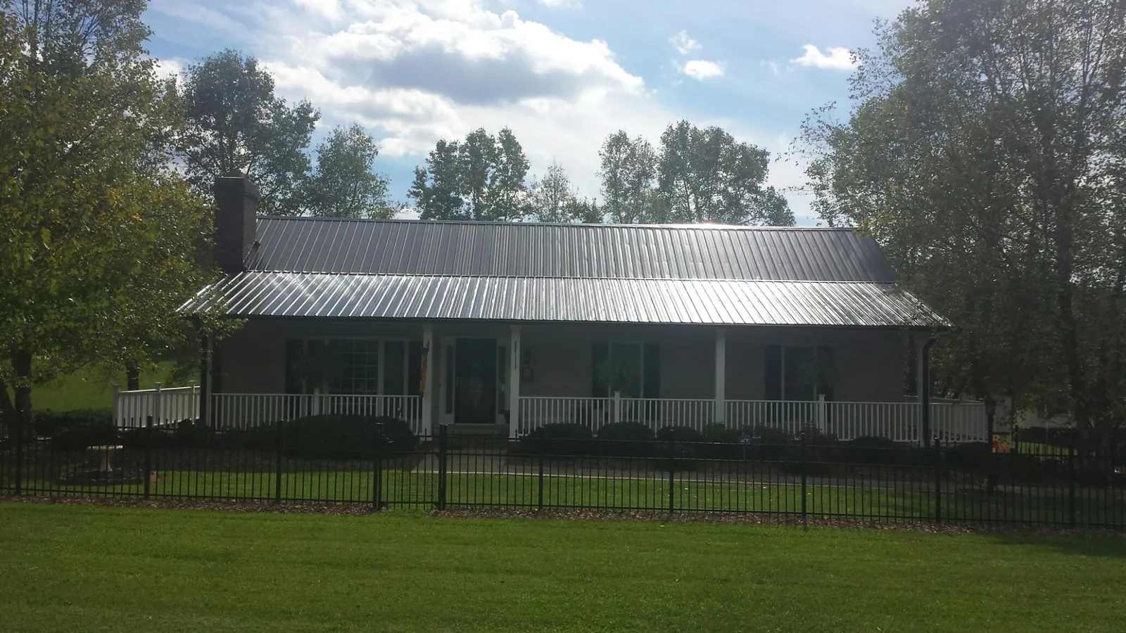Gray metal roof on a brick ranch with a full width front porch — Gutter Guard Installation work by our crew in Ira