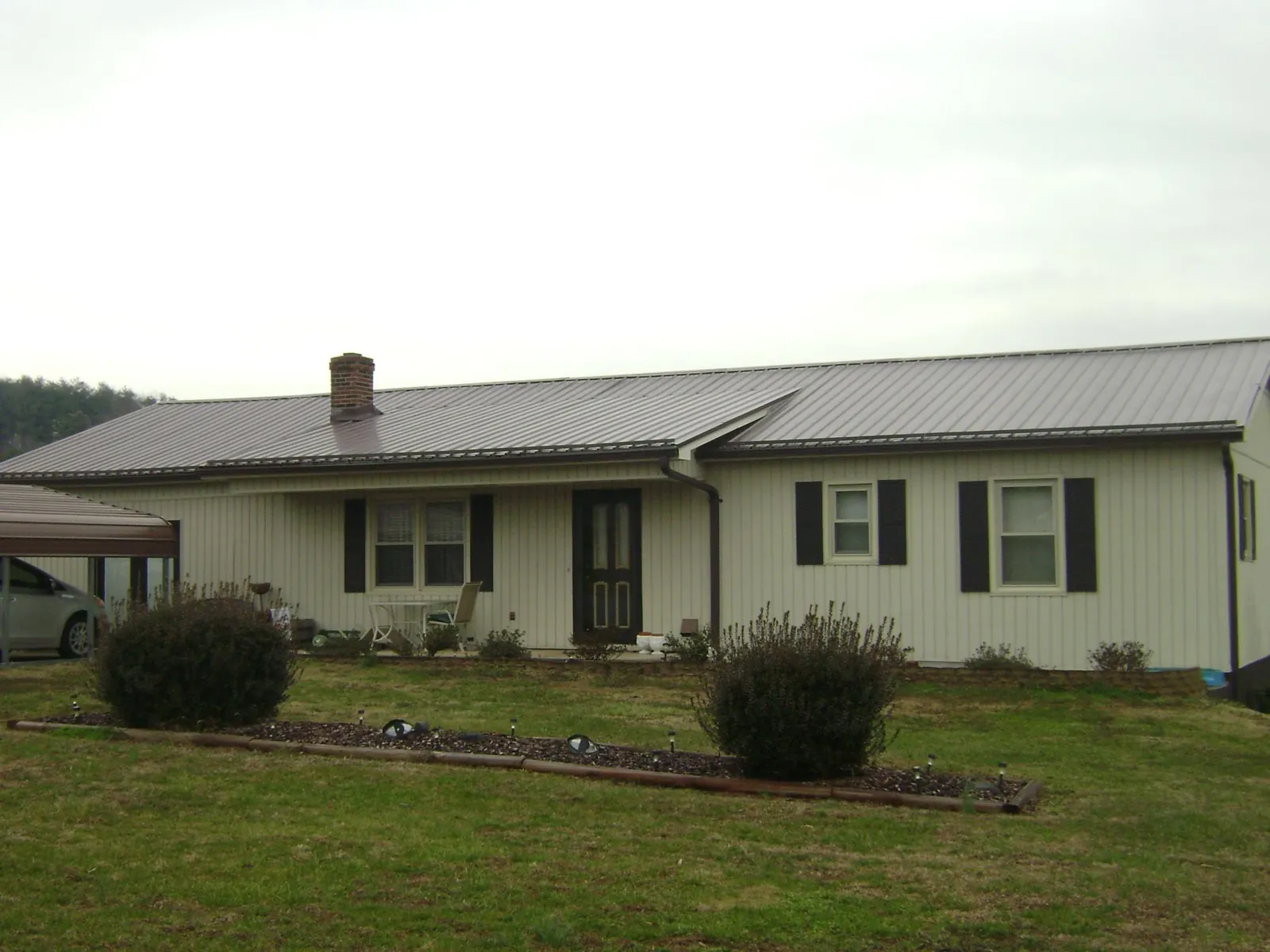 Brown metal roof on a cream sided ranch home with a brick chimney in Ira