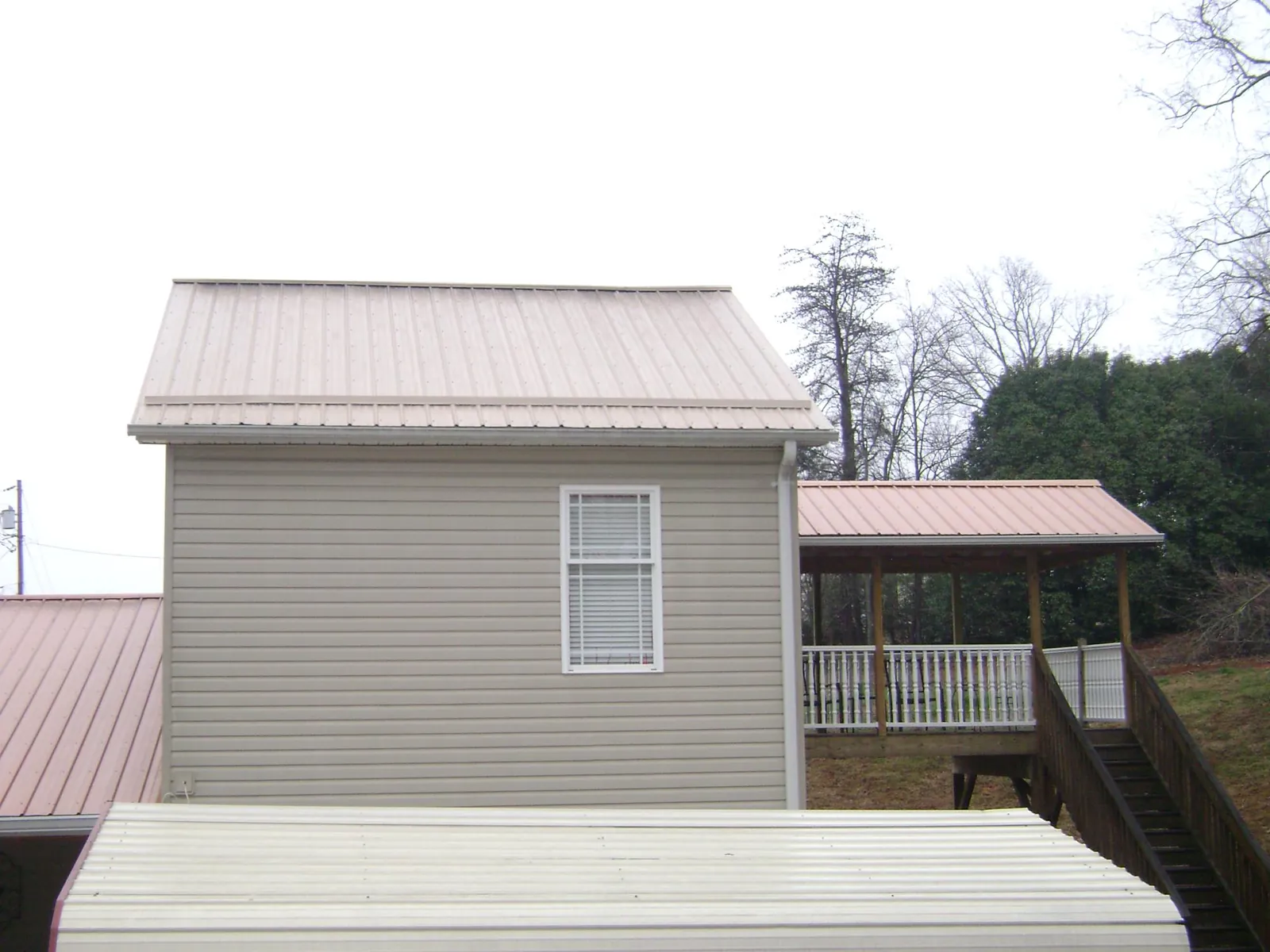 Tan metal roofs on a two story addition and attached porch, from a Roof Replacement job in Ira
